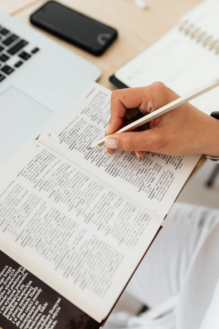 close up of woman sitting at the desk with a laptop and underlining words in a book